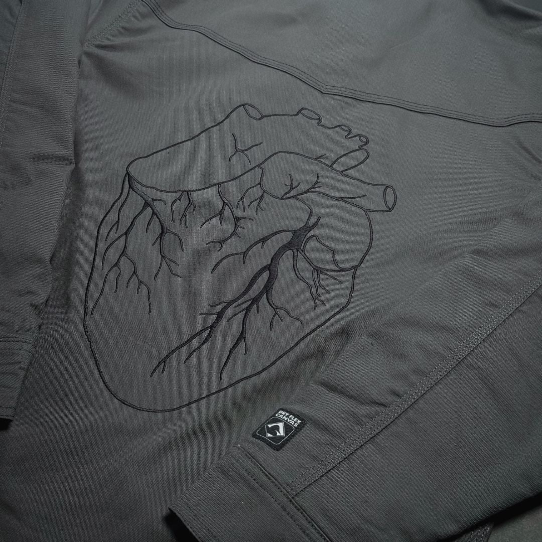 Dark gray work jacket with black embroidered anatomical heart design on chest from black gives way to blue collection