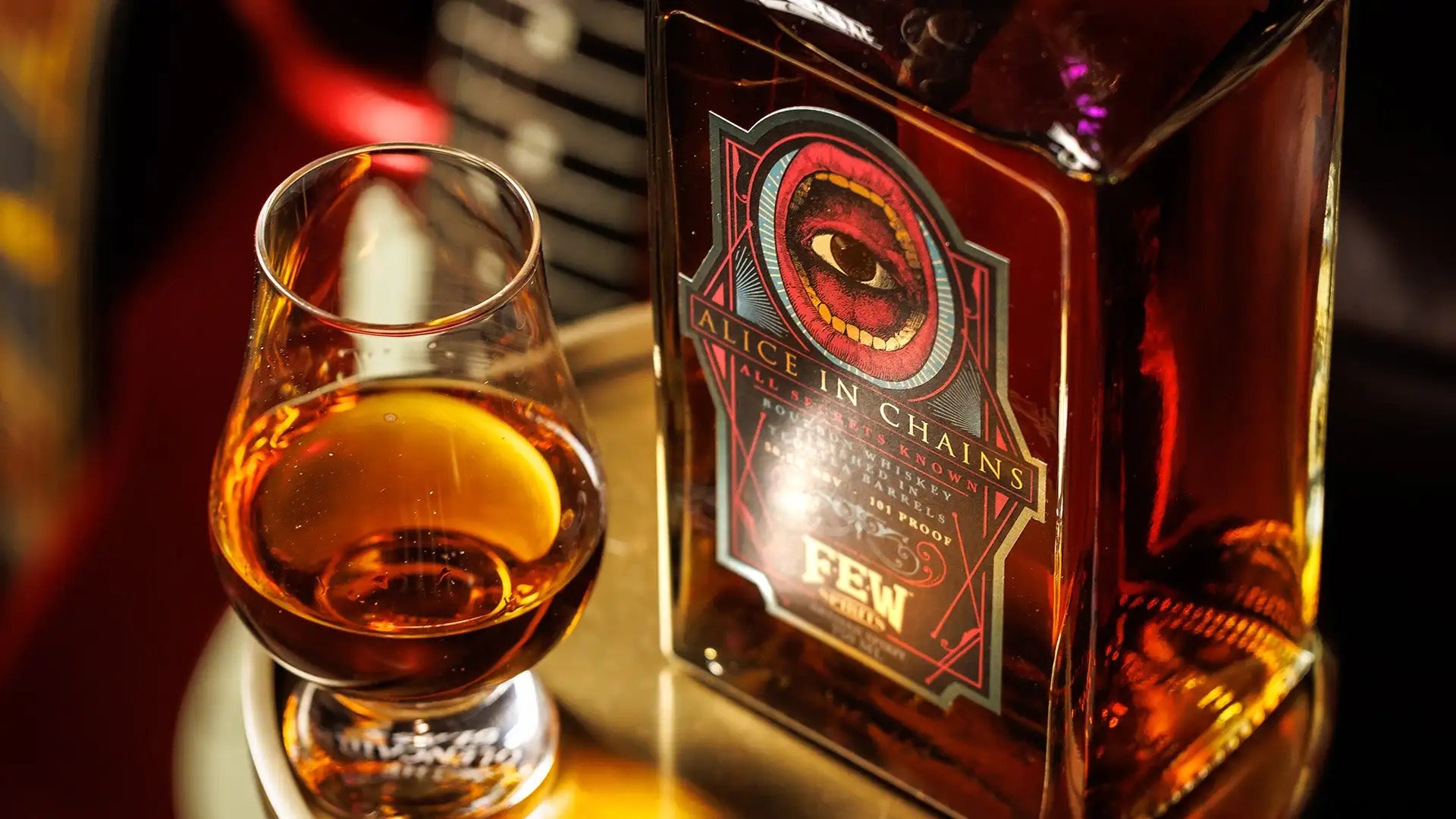 A rectangular glass bottle of alice in chains whiskey with a red and black label featuring an eye design, containing amber liquid.